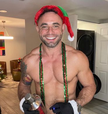 Smiling shirtless man wearing a Christmas hat and festive beads.
