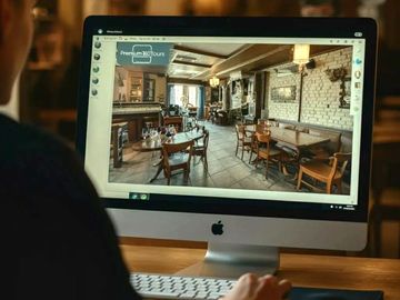 Person viewing a virtual tour of a cozy restaurant on an iMac.