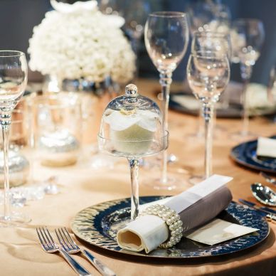 Elegant table setting with glassware, floral centerpiece, and a dessert under a glass dome.
