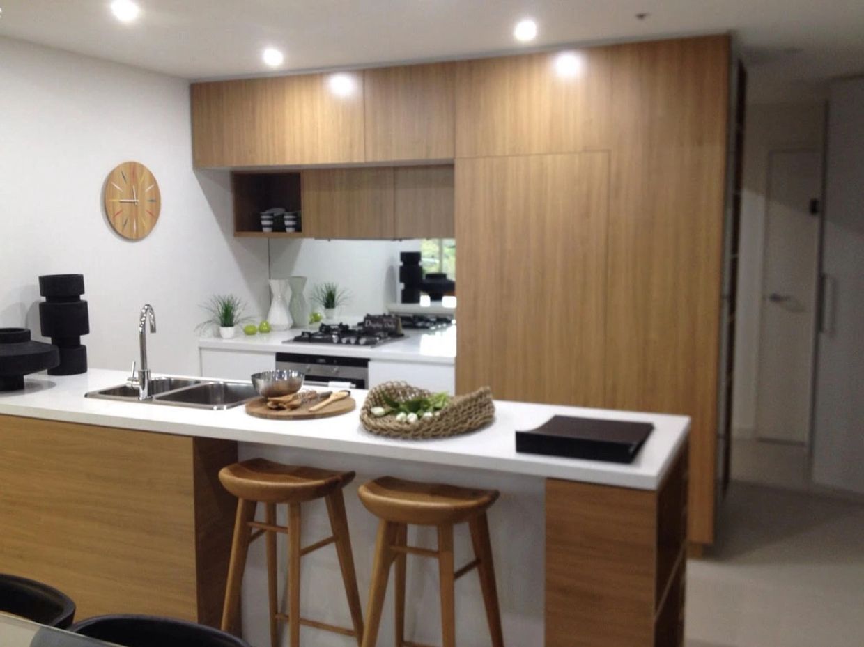 Modern kitchen with wooden cabinets and white countertops, featuring bar stools and decorative items.