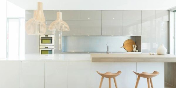 Minimalist white kitchen with wooden stools and pendant lights.