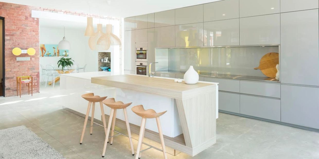 Bright modern kitchen with wooden island and stools, featuring sleek cabinetry and a cozy dining area.