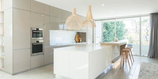 Modern kitchen with sleek cabinets, island, wooden stools, and large windows.