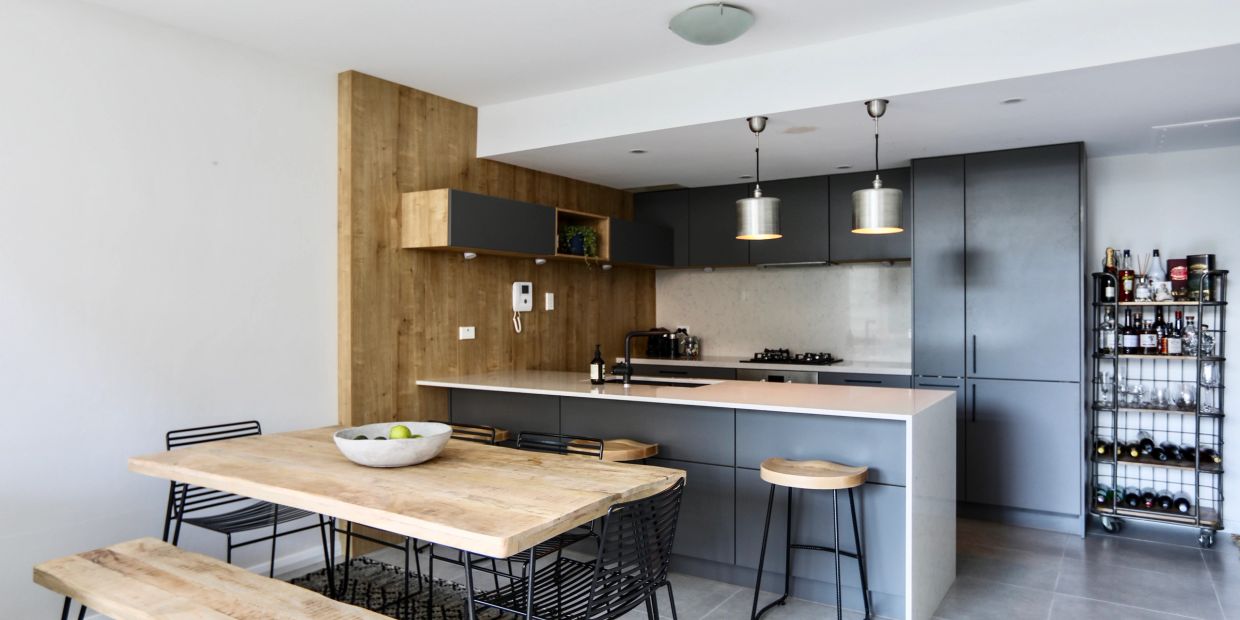 Modern kitchen with wooden and gray elements, featuring a dining table and bar stools.