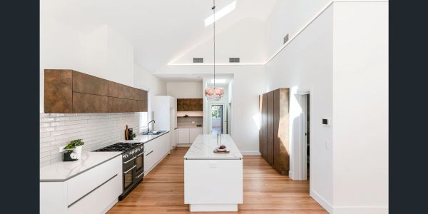Modern kitchen with white cabinets, wooden accents, and a central island under a high ceiling.