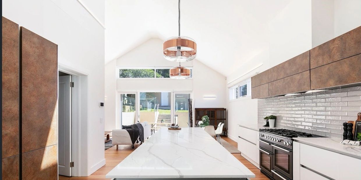 Bright modern kitchen with marble island and copper pendant lights.