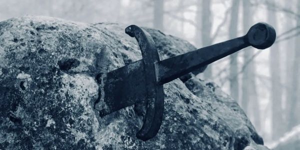 A sword embedded in a large rock in a misty forest.