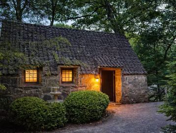 Cozy stone cottage with warm lights in a wooded setting.