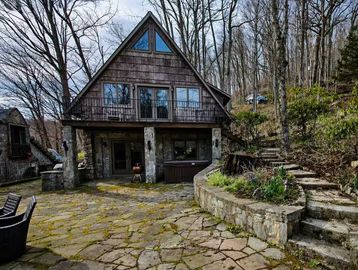 A-frame cabin in a wooded area with a stone patio.