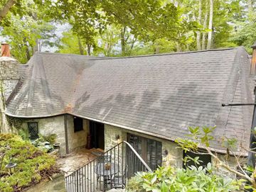 Charming stone cottage with a steep roof surrounded by greenery.