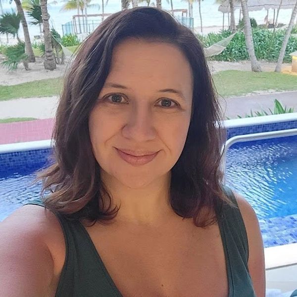 Woman smiling near a pool with palm trees in the background.