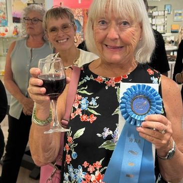 member celebrating with a wine glass and a blue ribbon.