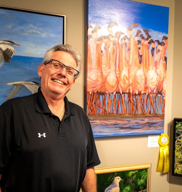 Artist in front of his picture of a group of flamingos 