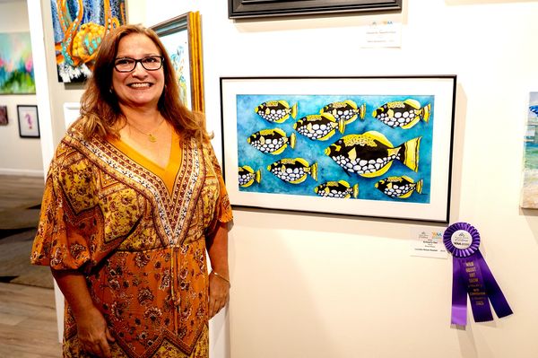 artist in front of her painting of a school of fish