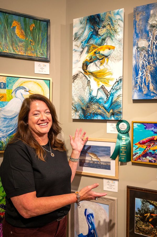 Artist in front of her picture of a yellow fish in water