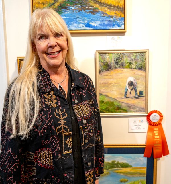 Artist in front of her painting of a person weeding in a garden