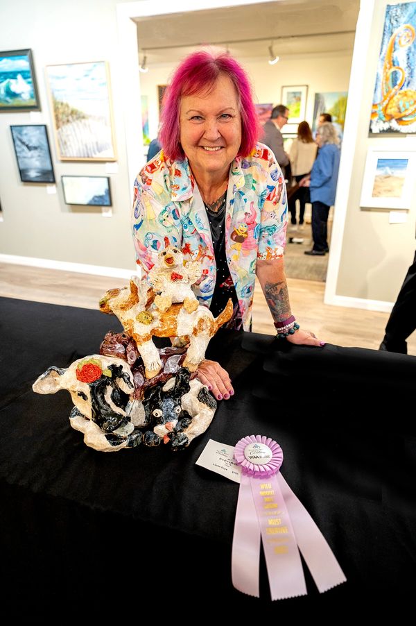 Artist in front of her 3D sculpture of whimsical barn animals stuck together