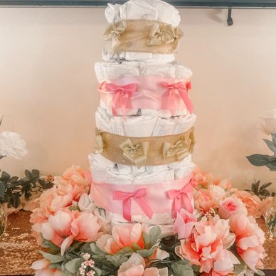 Decorative diaper cake adorned with ribbons and surrounded by flowers.