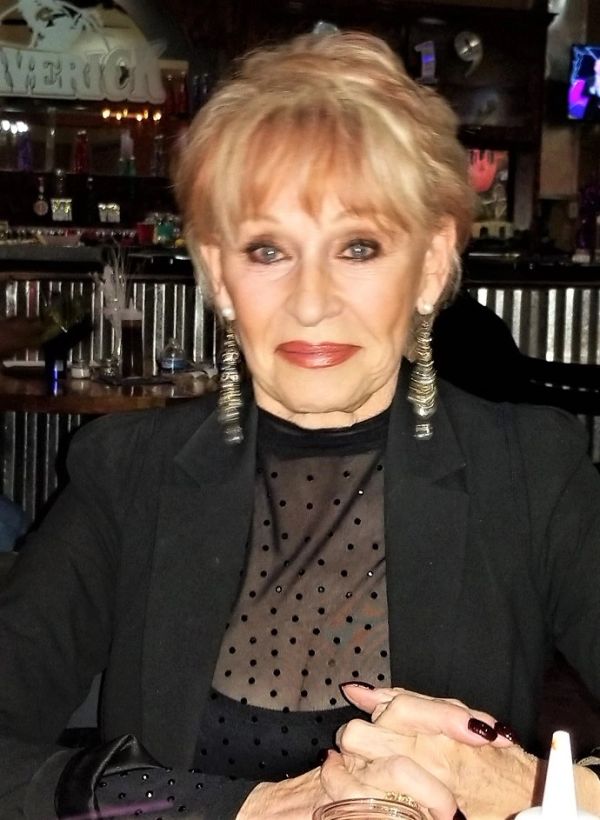 Elegant older woman with blonde hair and statement earrings.