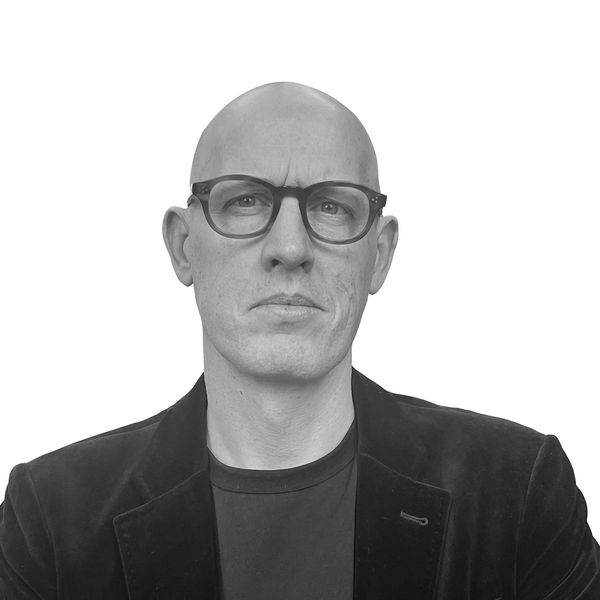 Serious bald man wearing glasses and a black jacket against white background.