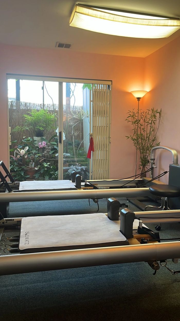 two Pilates reformers in a pink room with a garden