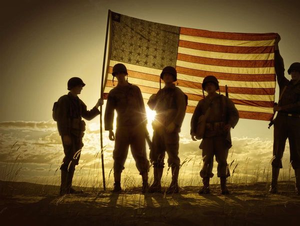 Silhouetted soldiers holding an American flag at sunset.