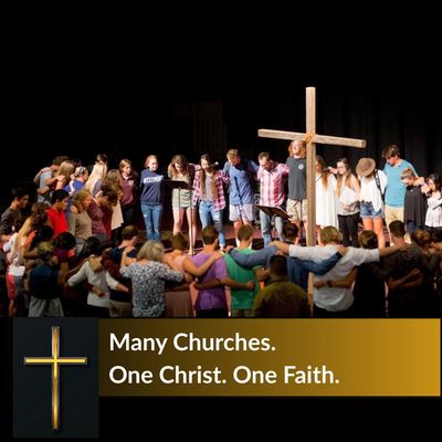 A diverse group gathers around a large cross in unity and faith.