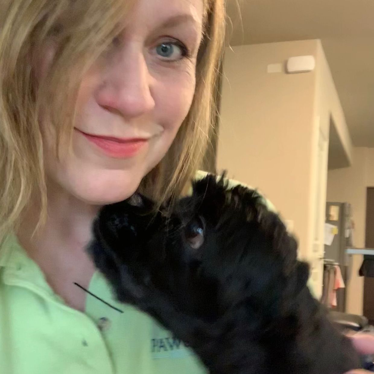 Woman smiling with a black dog close to her face.