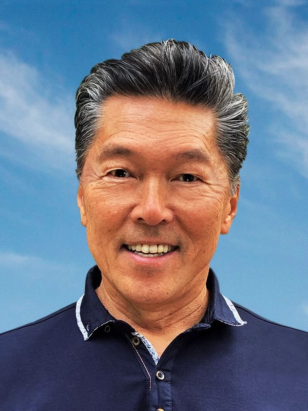 Smiling middle-aged man in a navy blue shirt against a clear blue sky.