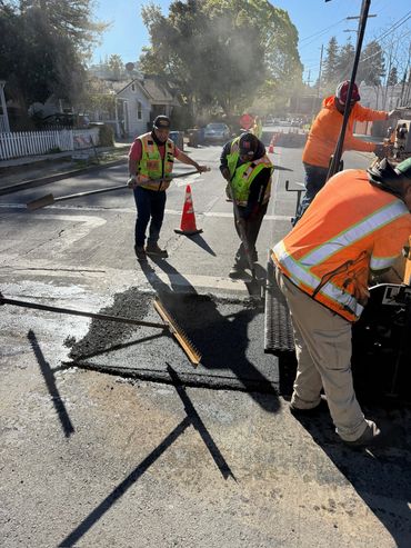 Workers repairing a street wearing safety vests and using tools in daylight.