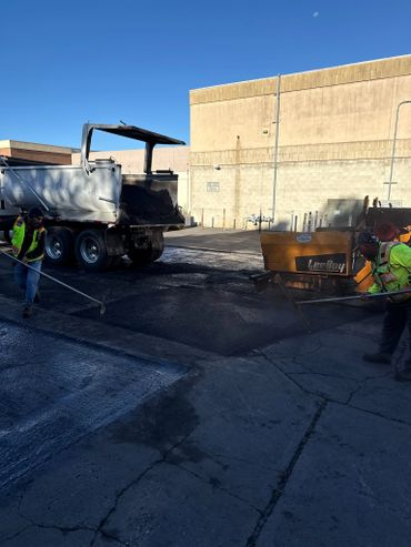 Workers paving asphalt on a concrete surface with machinery under clear blue sky.
