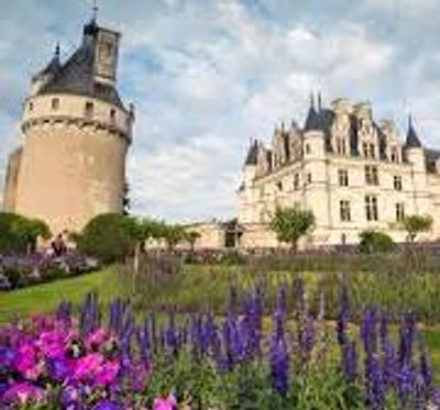 Historic castle with colorful flower garden in front under a partly cloudy sky.