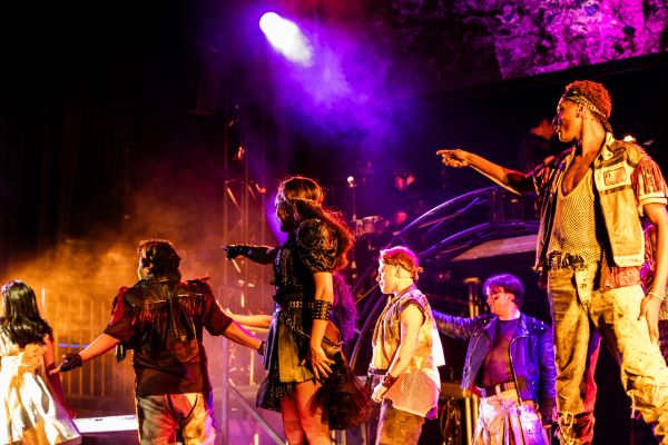Actors performing a dramatic scene on stage with vibrant lighting.