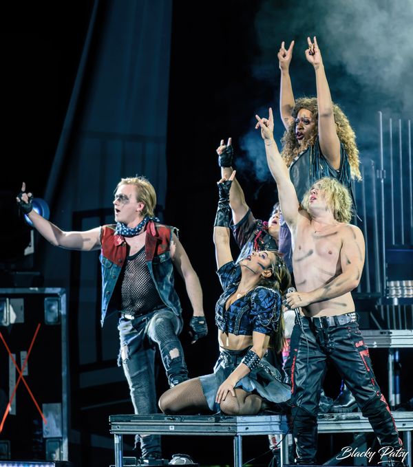 Rock band performing energetically on stage with dramatic poses and outfits.