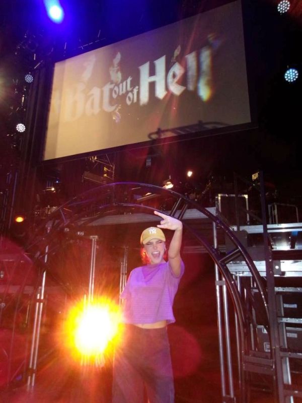 Person posing energetically in front of a 'Bat Out of Hell' sign with bright stage lights.