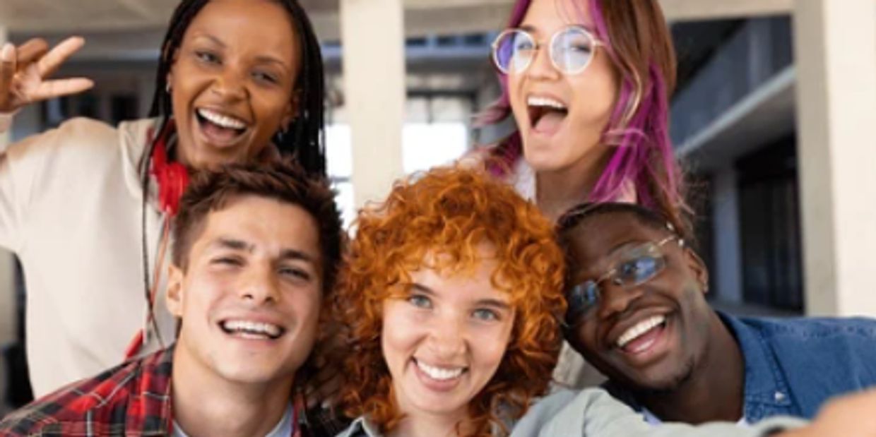 A group of five friends smiling and posing for a selfie indoors.