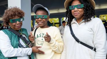 Three people wearing green eclipse glasses and smiling.