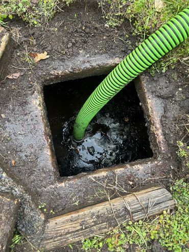 Green hose inserted into muddy water in a square pit outdoors.