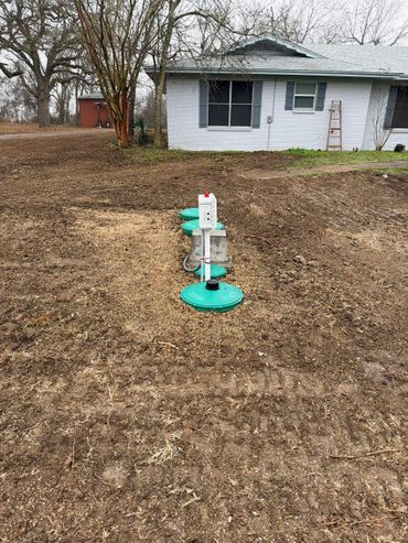 New septic system installation with green lids in front of a white house.