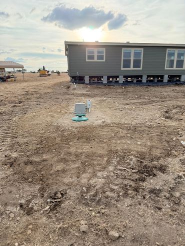 A modular home on stilts with exposed foundation and utility connections in dry land.