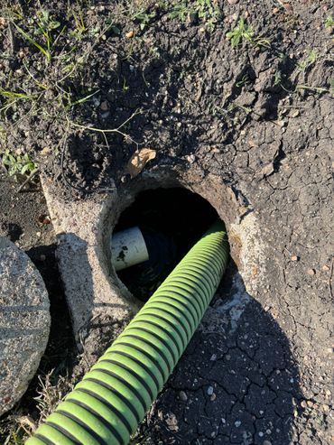 Green flexible pipe going into a round underground concrete hole with dry soil around.