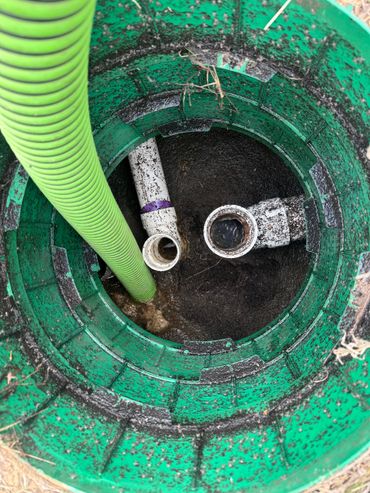 Inside view of a green plastic septic tank with pipes and a green hose.