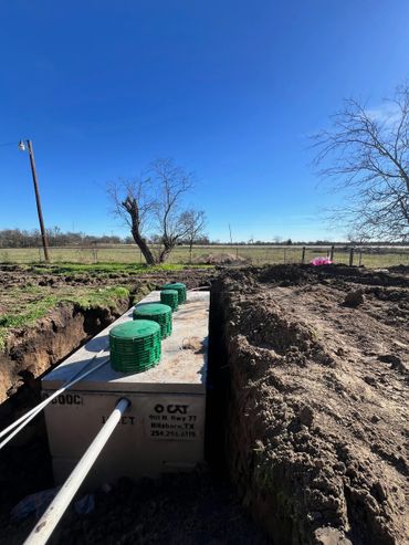 Concrete septic tank installation in a rural setting under a clear blue sky.