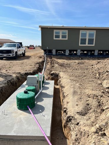 Septic system installation near a raised house with a truck nearby.