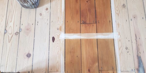 Wooden floor with a taped rectangular section showing a darker wood tone.