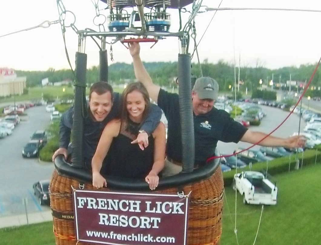 Three people enjoying a hot air balloon ride over a parking lot.