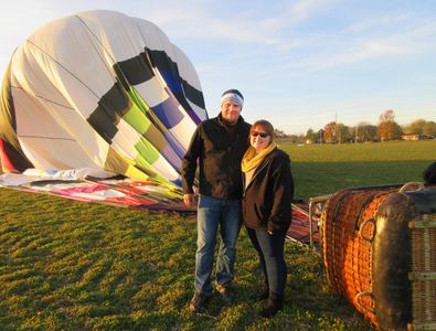 Couple posing beside a partially deflated hot air balloon on a grassy field.