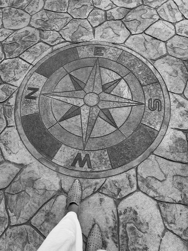 A colorful compass rose embedded in stone pavement beside a person's feet.