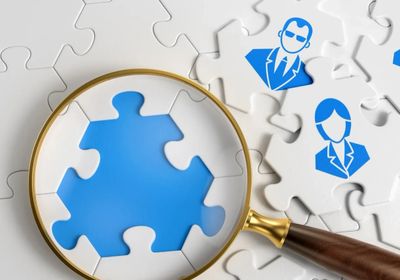 Magnifying glass highlighting a missing puzzle piece with business icons on other pieces.