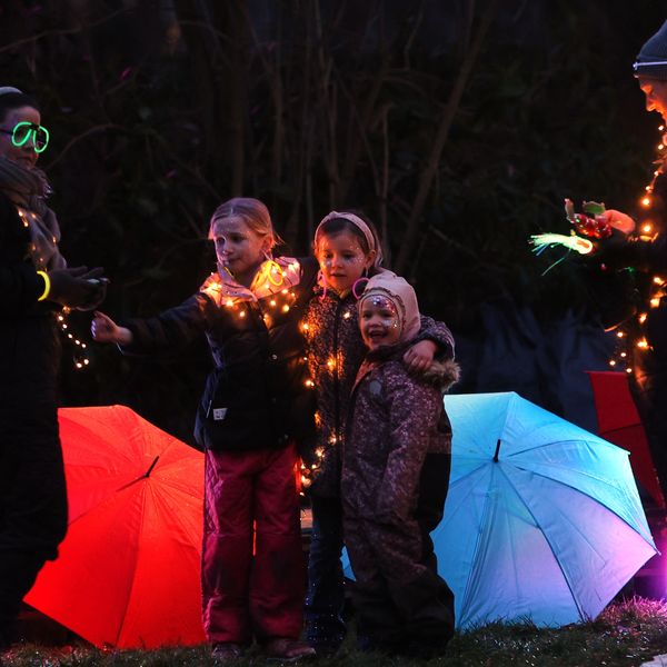 Children wrapped in fairy lights stand between glowing umbrellas at night.